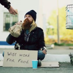Homeless individual with 'Will Work For Food' sign receives help outdoors. — Kia Syros Safety Features: Crash Tests, Ratings,