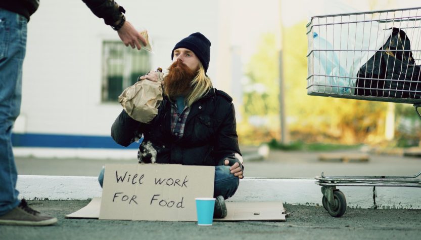 Homeless individual with 'Will Work For Food' sign receives help outdoors. — Kia Syros Safety Features: Crash Tests, Ratings,