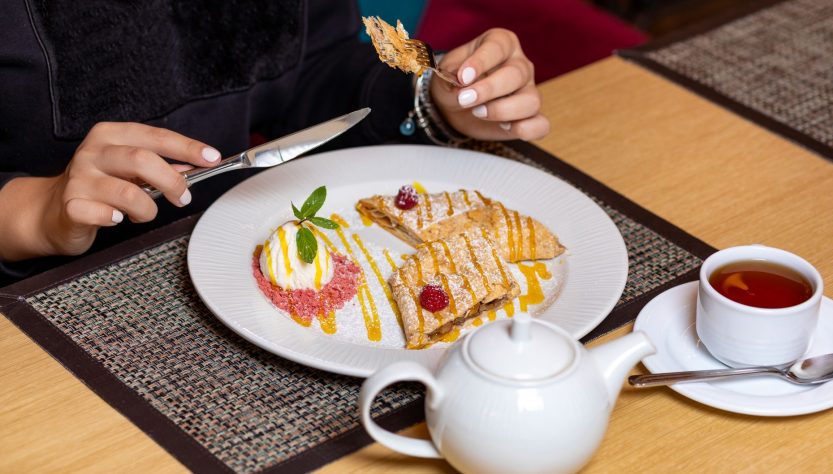 A close-up of a person enjoying a delicious dessert and tea in a cozy setting. — The Financial Perspective and Industry Knowl
